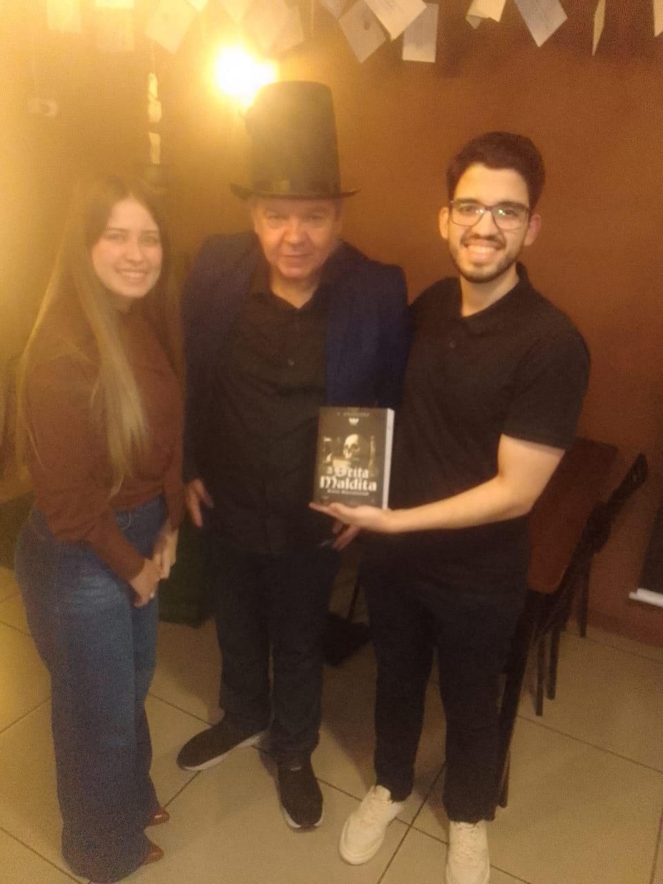 J. Angelini de cartola com um casal, o leitor segura A Seita Maldita