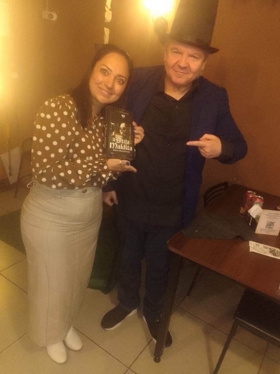 J. Angelini de cartola e leitora segurando A Seita Maldita