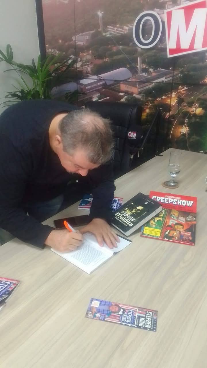 autor autografando livro em sessão de autógrafos, com obras de Stephen King na mesa