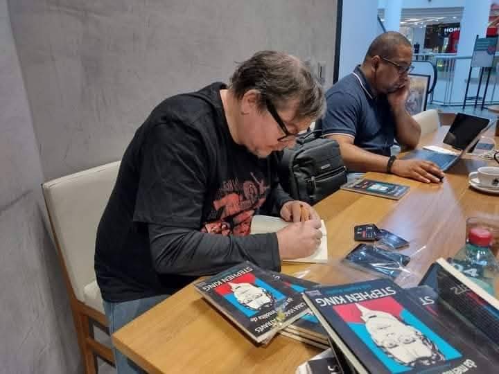 autor autografando livros em evento literário, com exemplares sobre a mesa