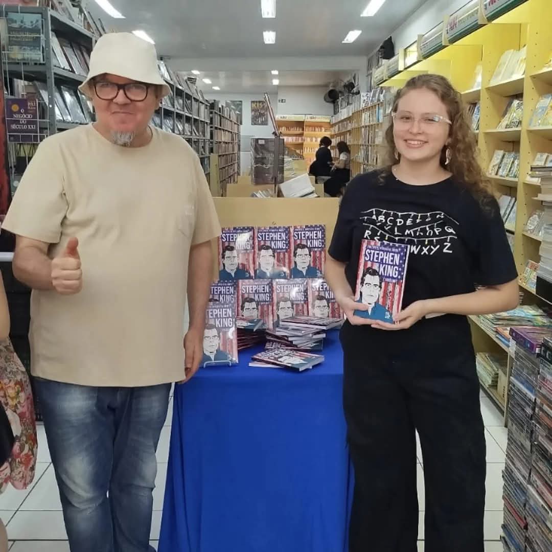 autor em livraria ao lado de mesa com livros de terror